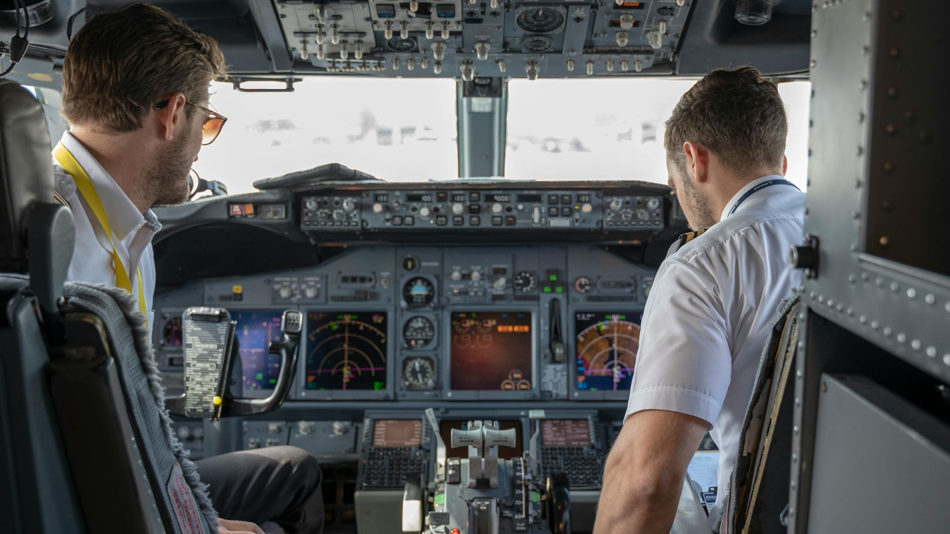 Two pilots navigating an aircraft cockpit, focused on advanced avionics and flight systems.