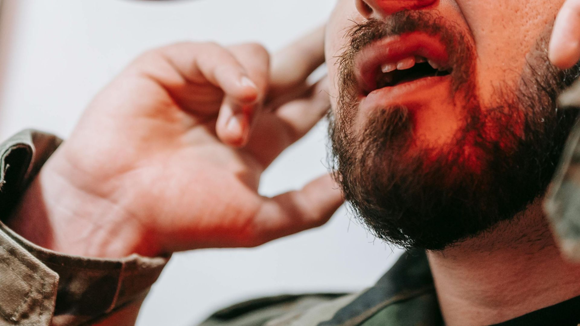 A close-up view of a bearded man talking with hands near his face.