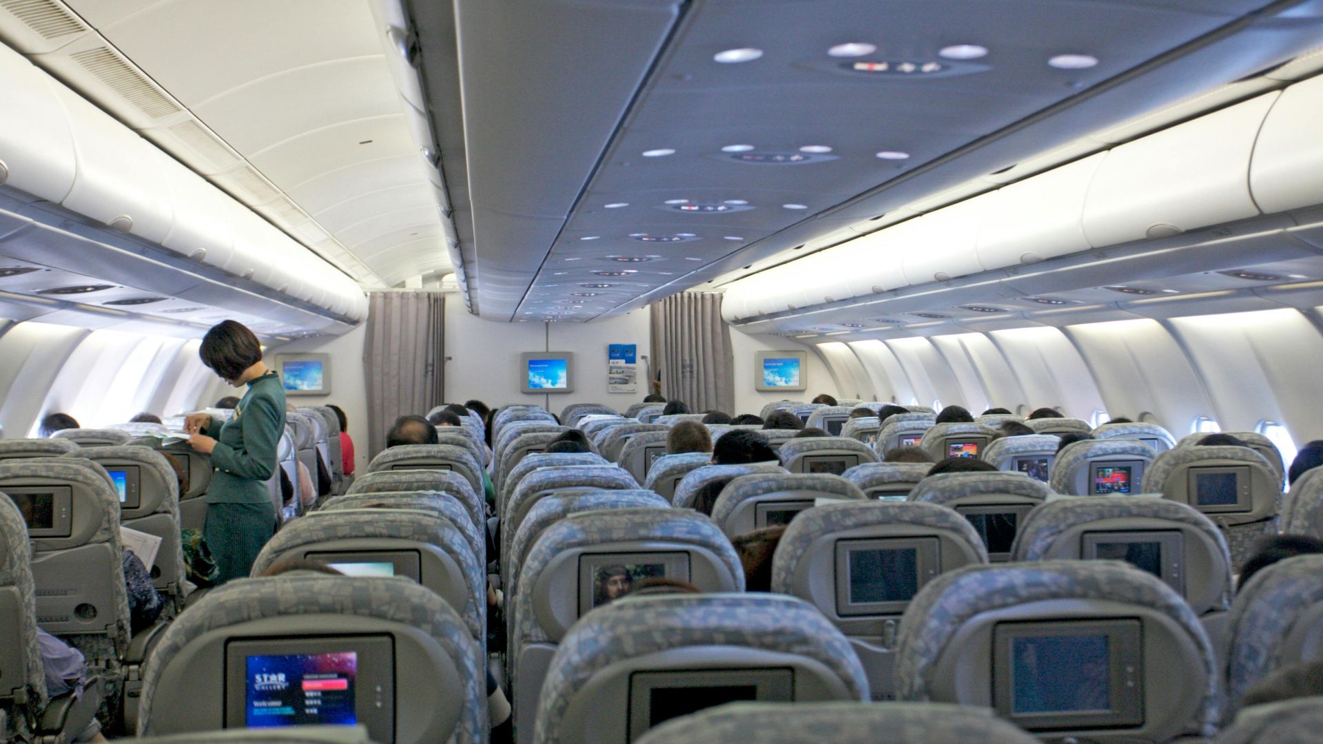 Interior view of a commercial airplane filled with passengers and cabin crew attending to travelers.