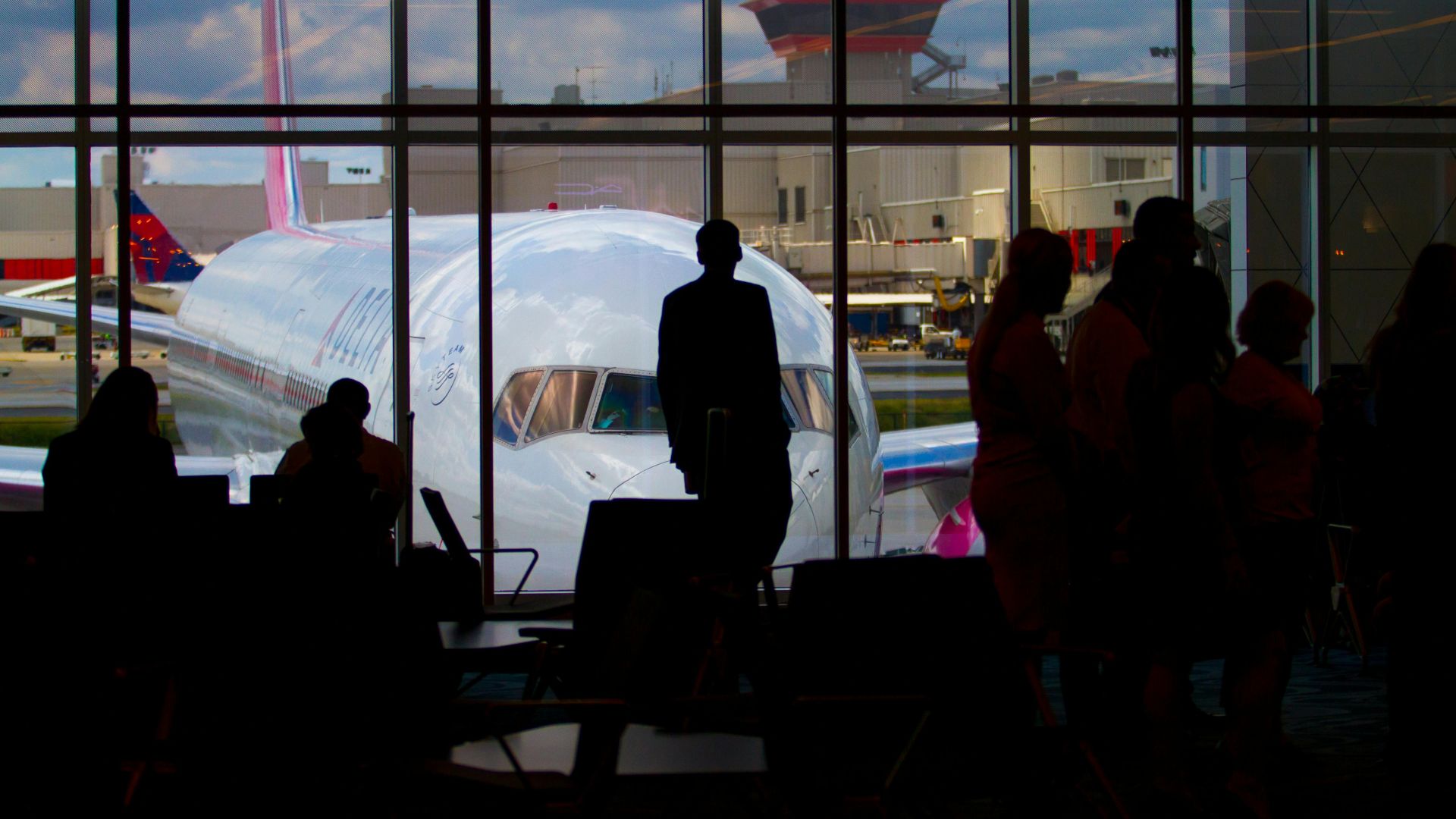 Silhouettes of travelers waiting at an airport terminal with an airplane visible through the window.