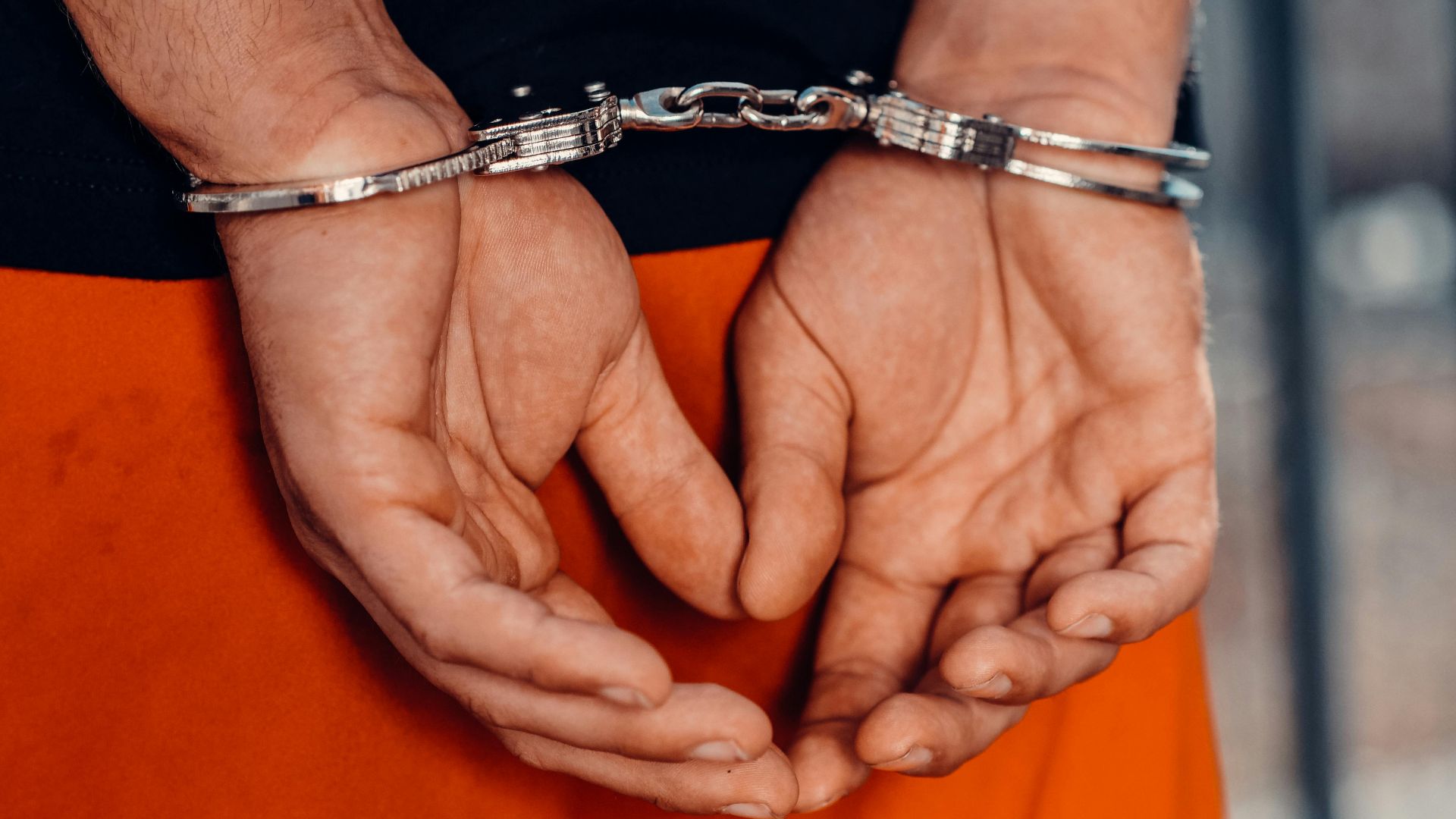 Rear view of handcuffed person in orange uniform, highlighting law enforcement and justice themes.