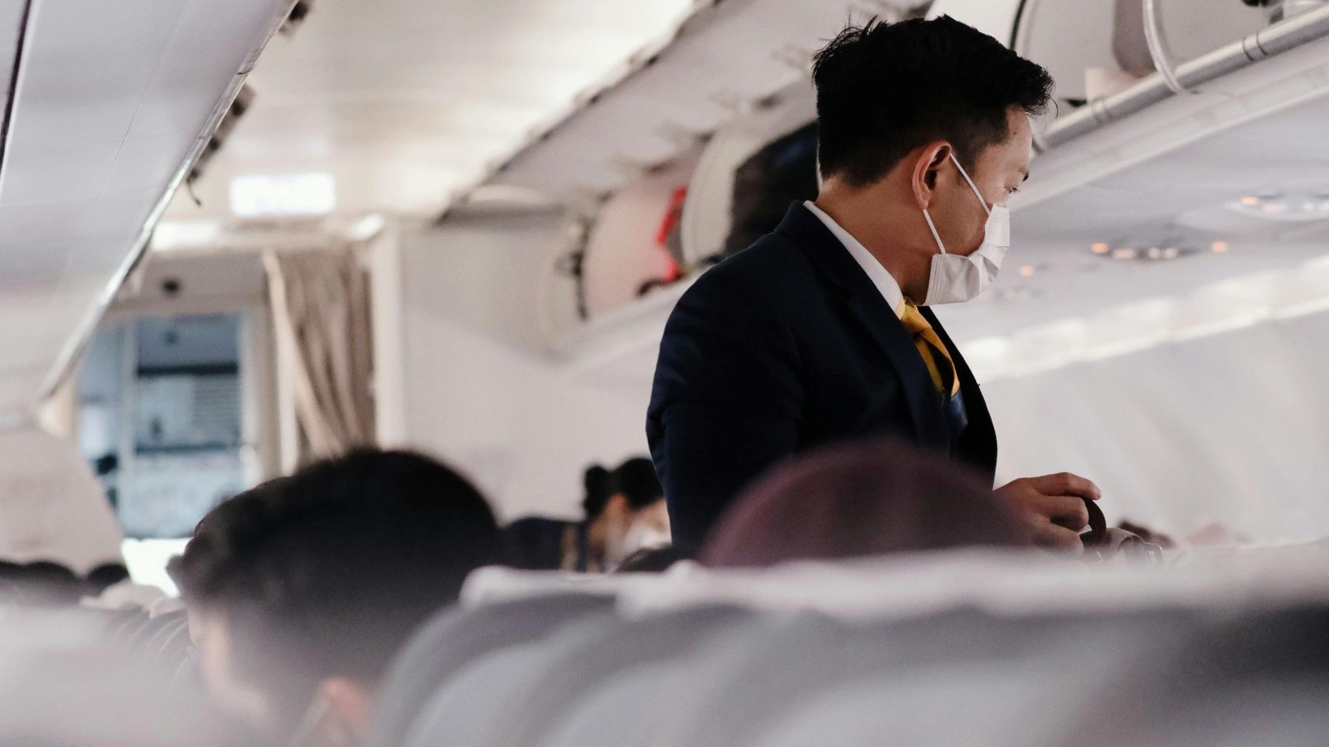 A flight attendant wearing a mask assists passengers on a commercial flight.