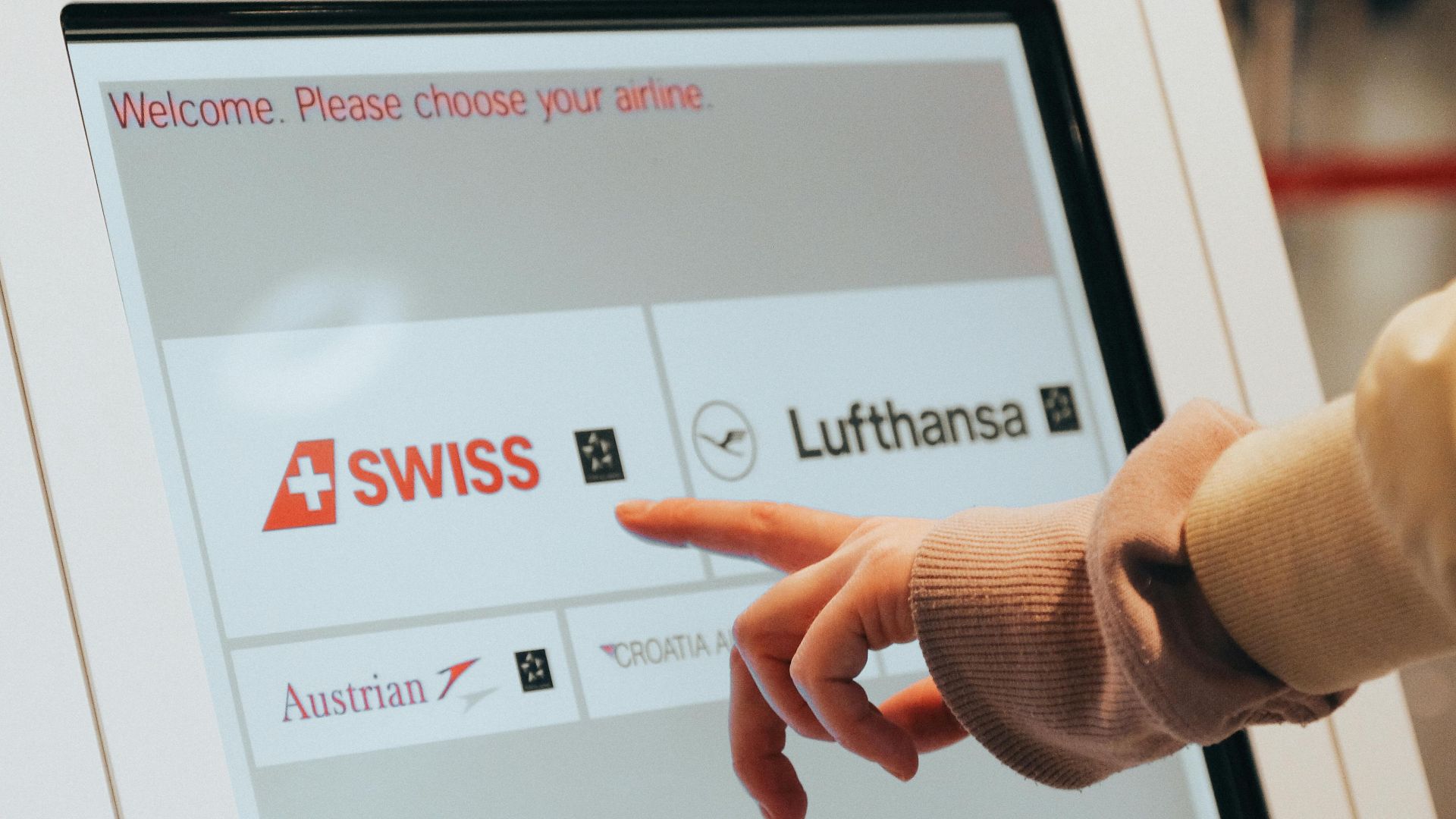 Hand interacting with airport kiosk for airline selection. Modern travel technology.