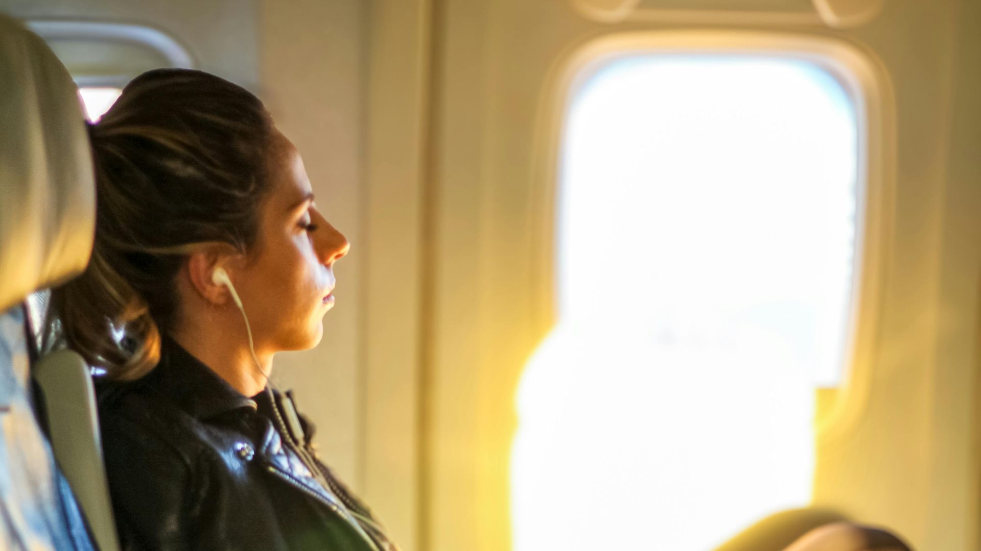 A woman enjoys a tranquil moment on a flight, gazing out the window with headphones on.
