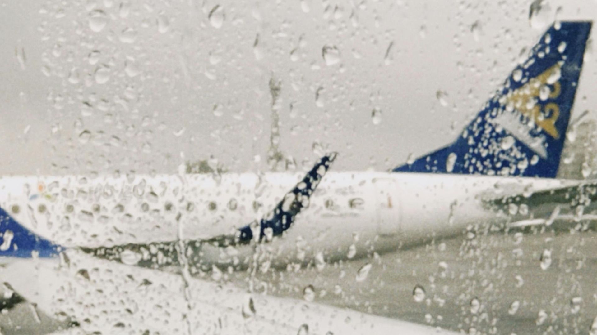 A rainy day view from an airplane window showing the wing and airport surroundings.
