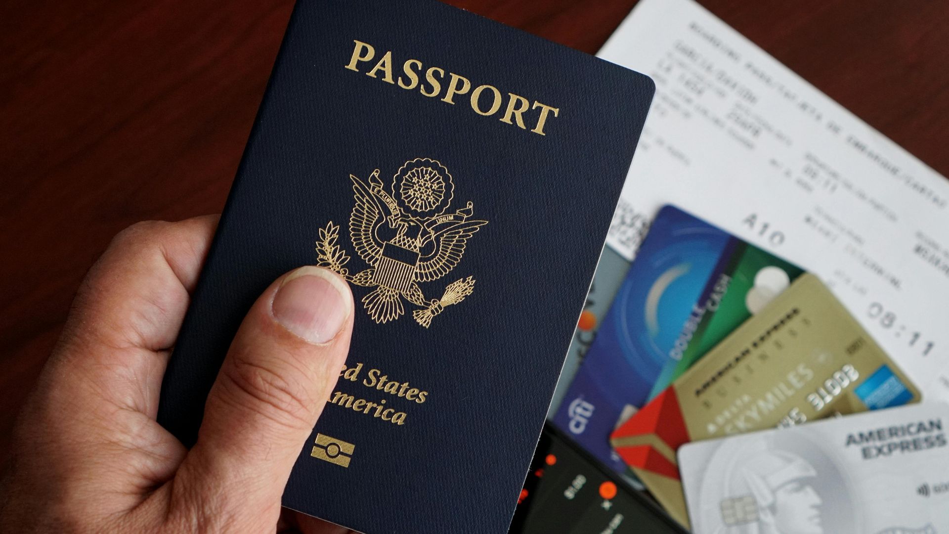 A close-up of a US passport with credit cards, tickets, and a mobile phone on a table.