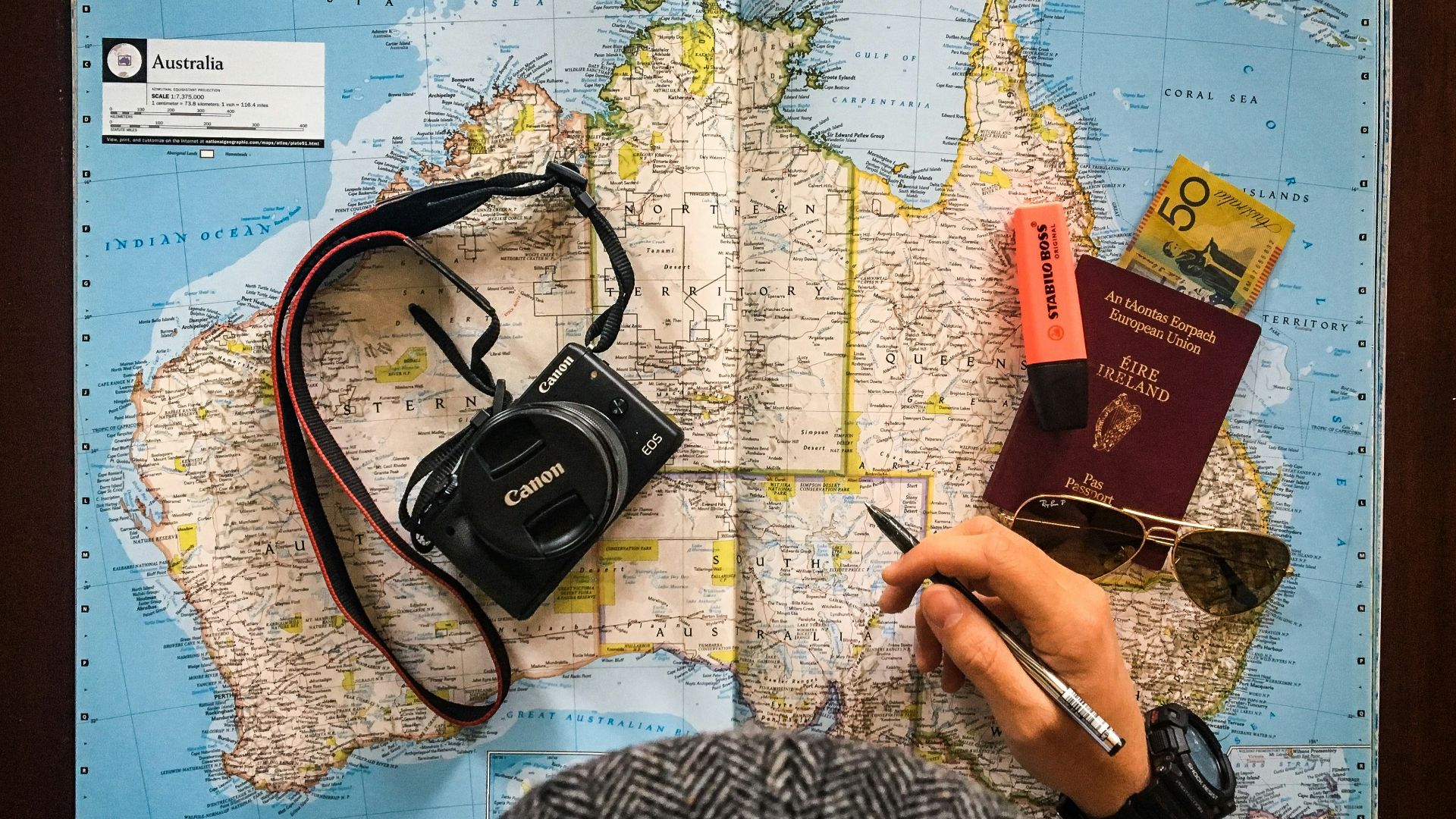 flat lay photography of person holding pen in front of world map