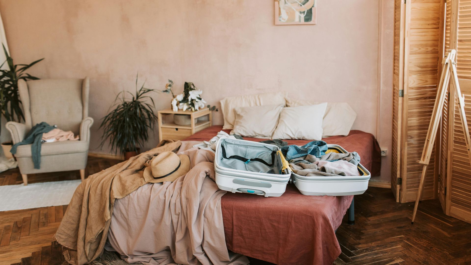Open suitcase on a bed in a cozy, warmly decorated bedroom, ready for travel.