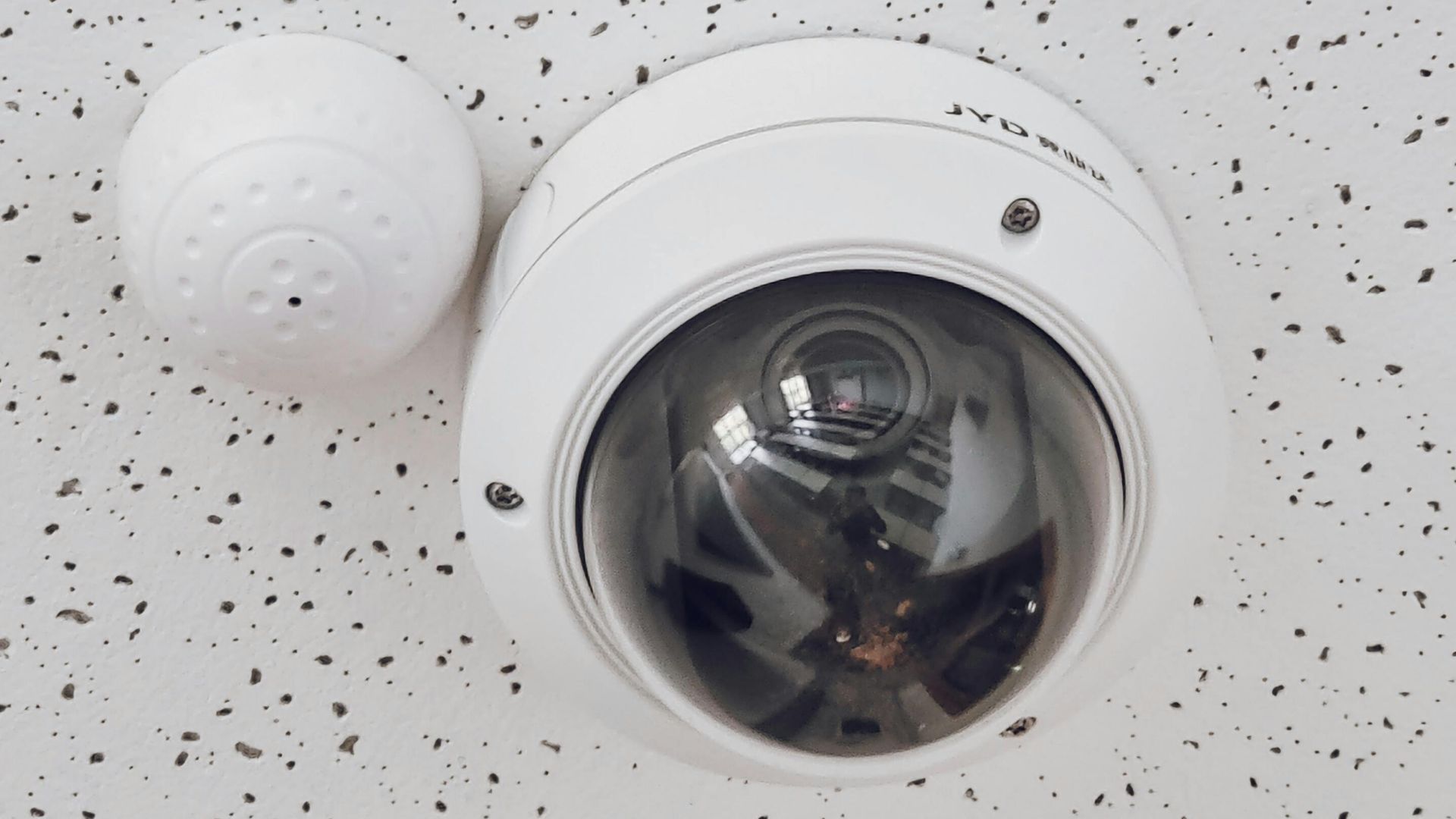Close-up of a round dome surveillance camera installed on a speckled ceiling for security monitoring.