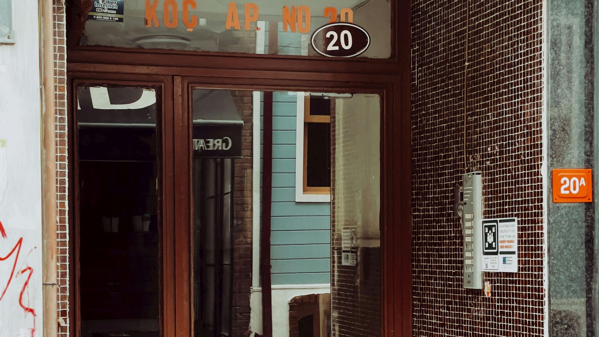 A brown entrance door of an urban apartment building with reflections and street views.