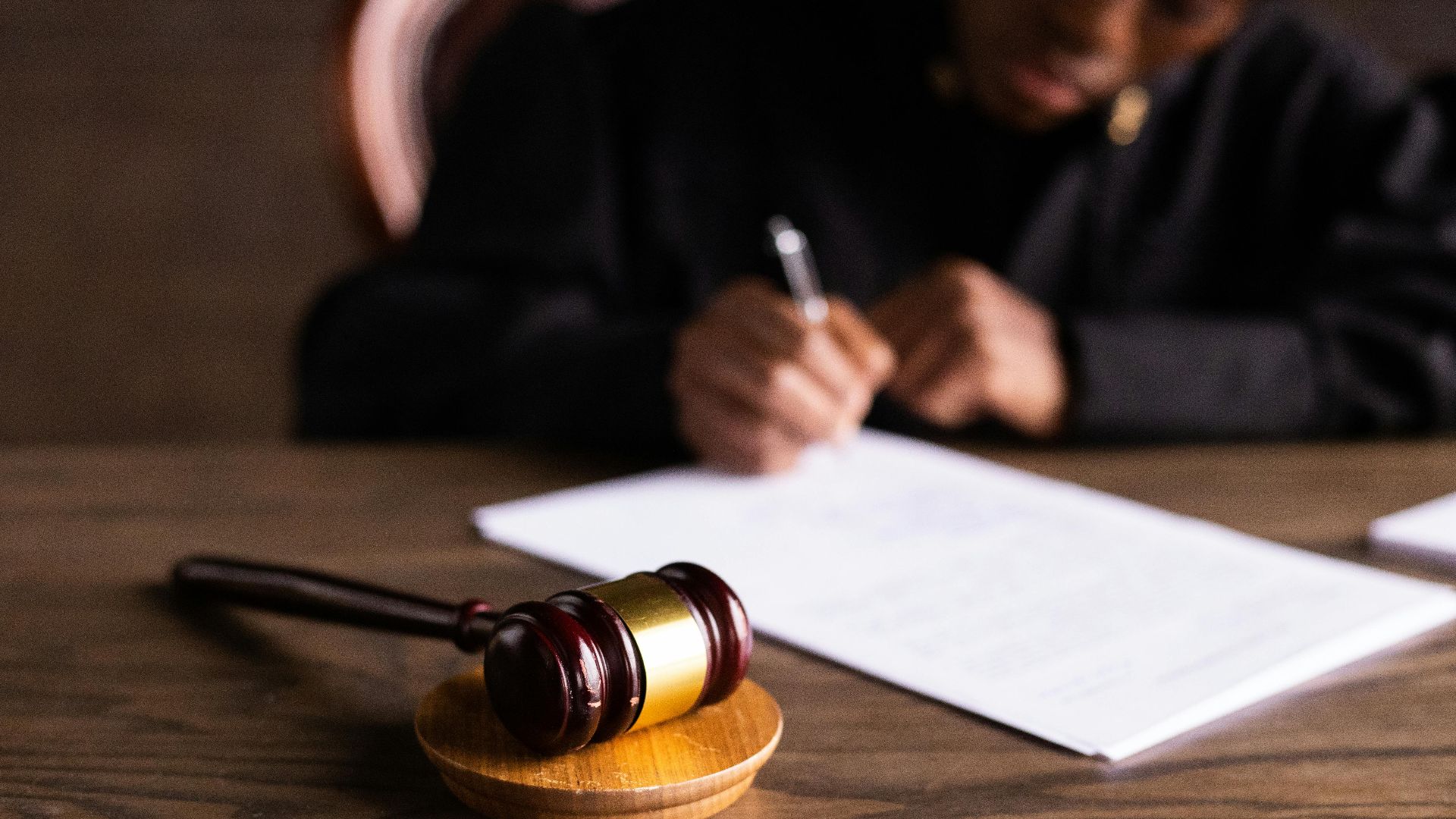 Judge signing documents at desk with focus on gavel, representing law and justice.