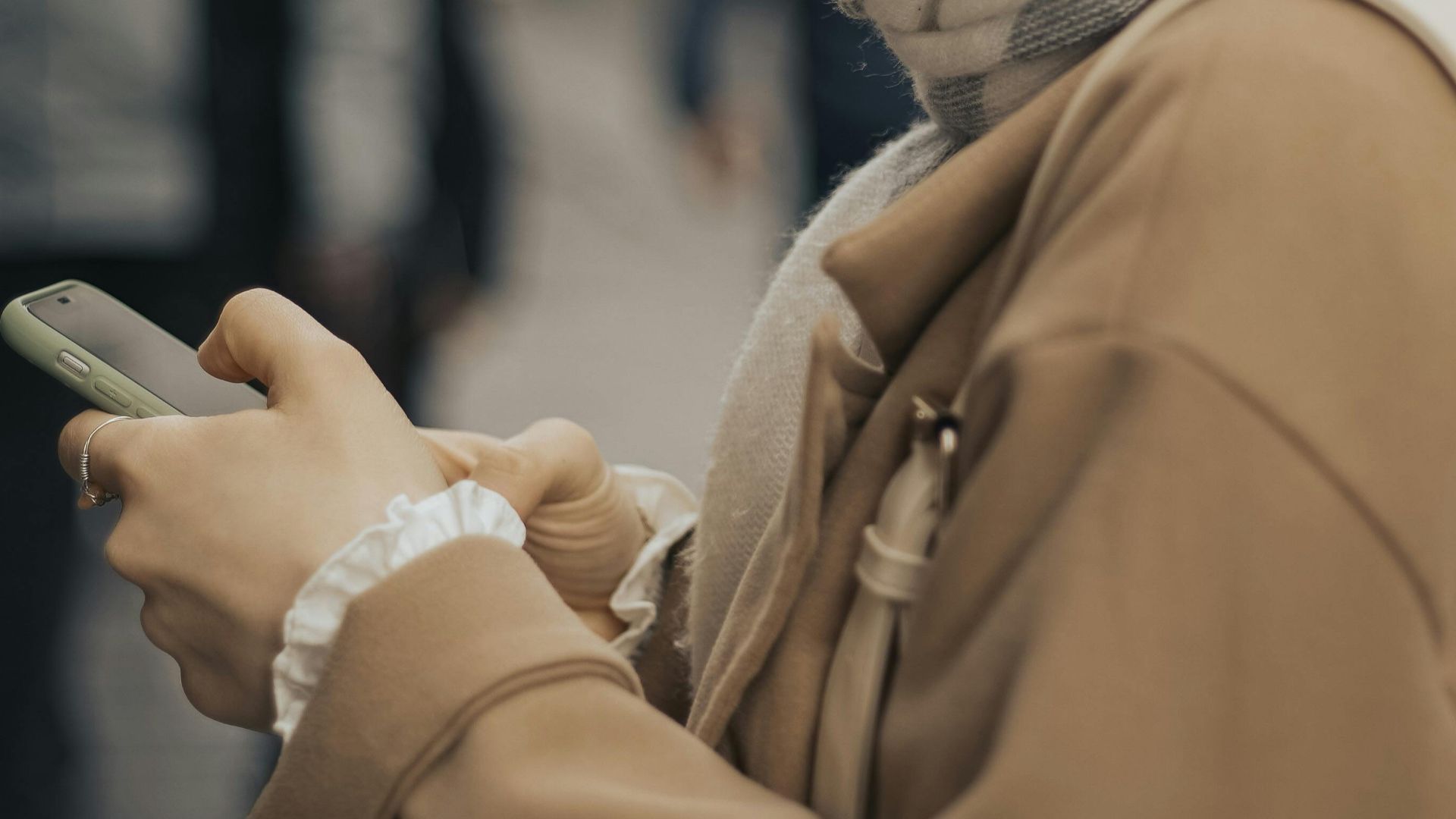 Close-up of a woman in a coat using a smartphone on an urban street.