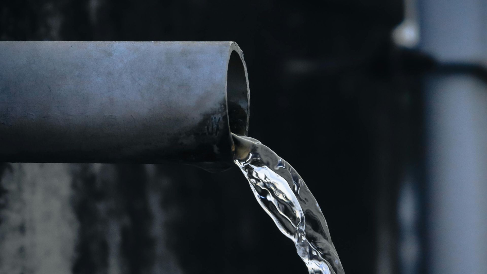 Close-up view of water pouring from an industrial metal pipe, captured outdoors.