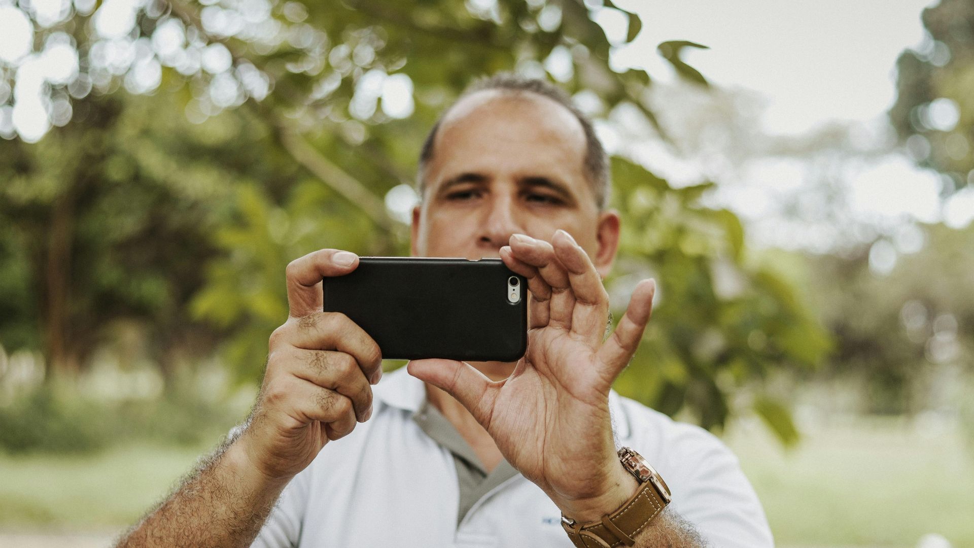 Adult man using smartphone to take a photo in a natural setting, showcasing modern technology and leisure.
