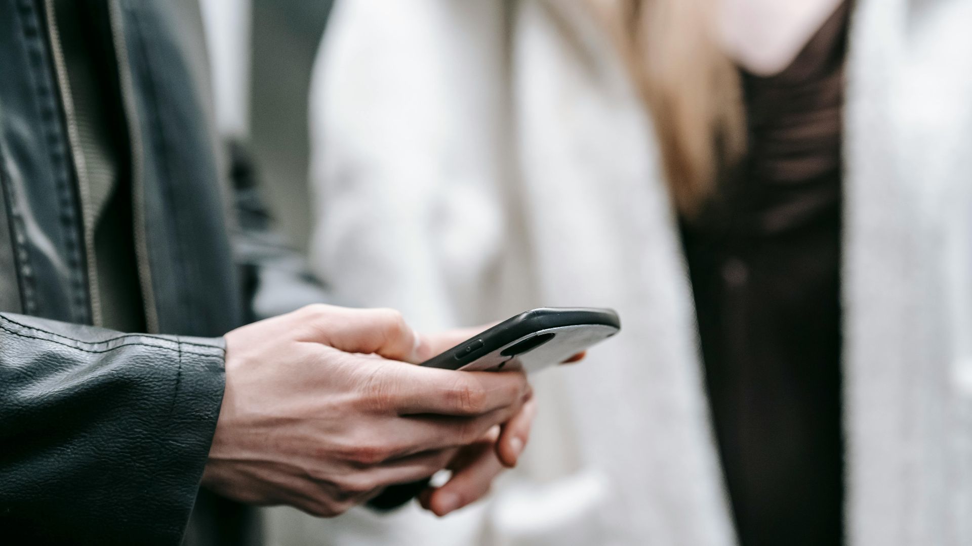 Crop faceless couple in warm clothes standing together while text messaging on phone