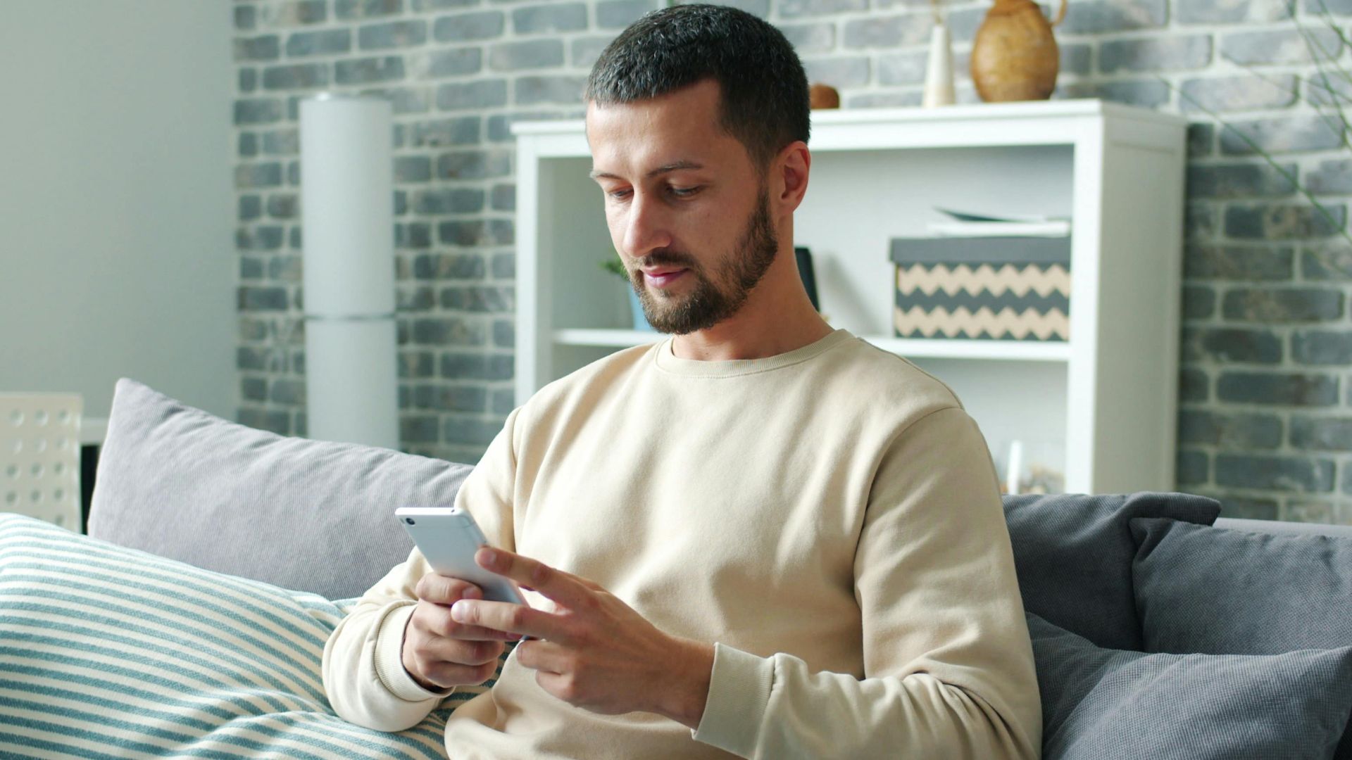 Man sitting on a couch using a smartphone in a cozy living room setting.