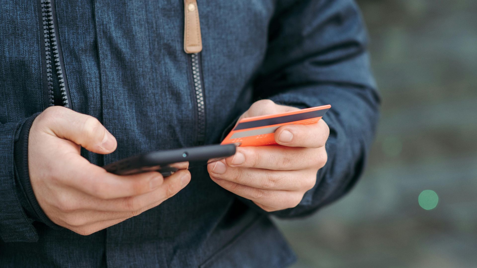 Crop anonymous male in casual clothes entering credit card details on smartphone on street in daylight