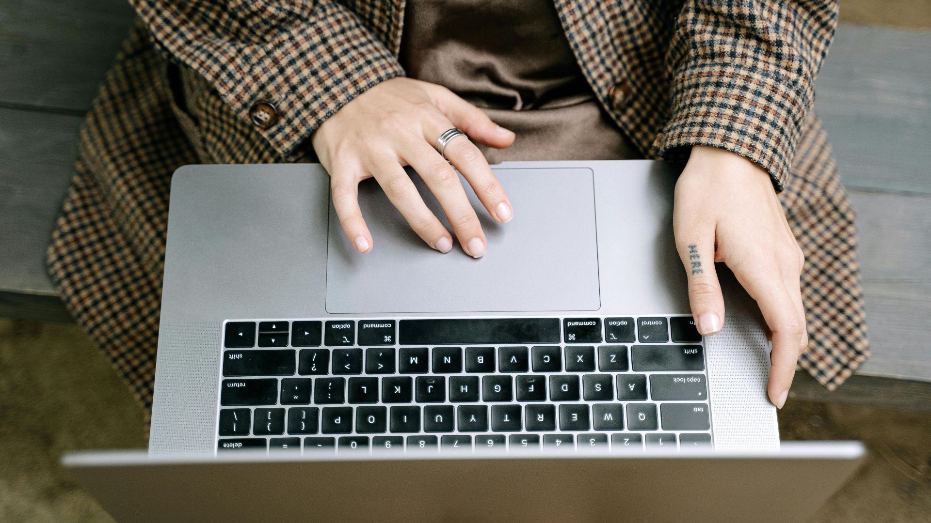 High angle view of individual using a laptop on a wooden bench while wearing a checkered coat.