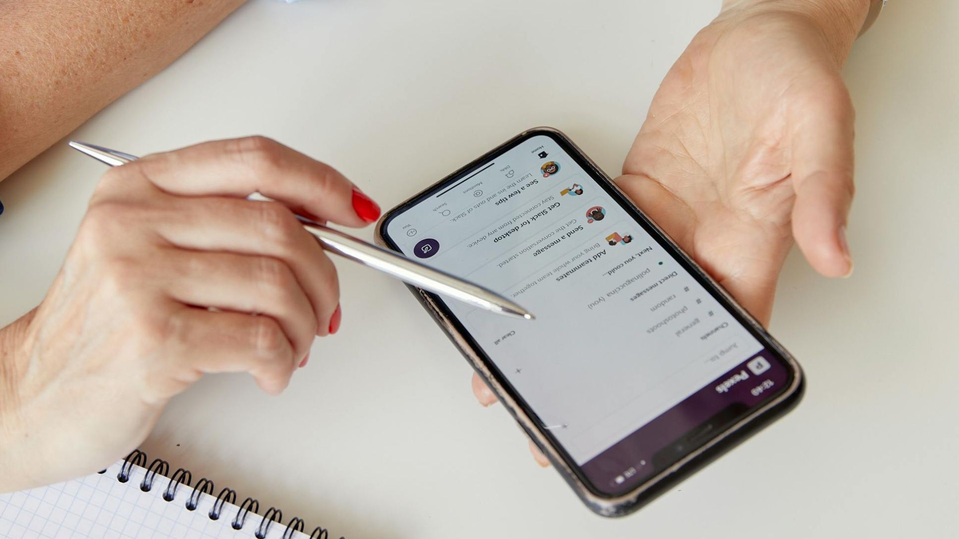 Two adults collaborate using a smartphone and a notepad in an indoor setting.
