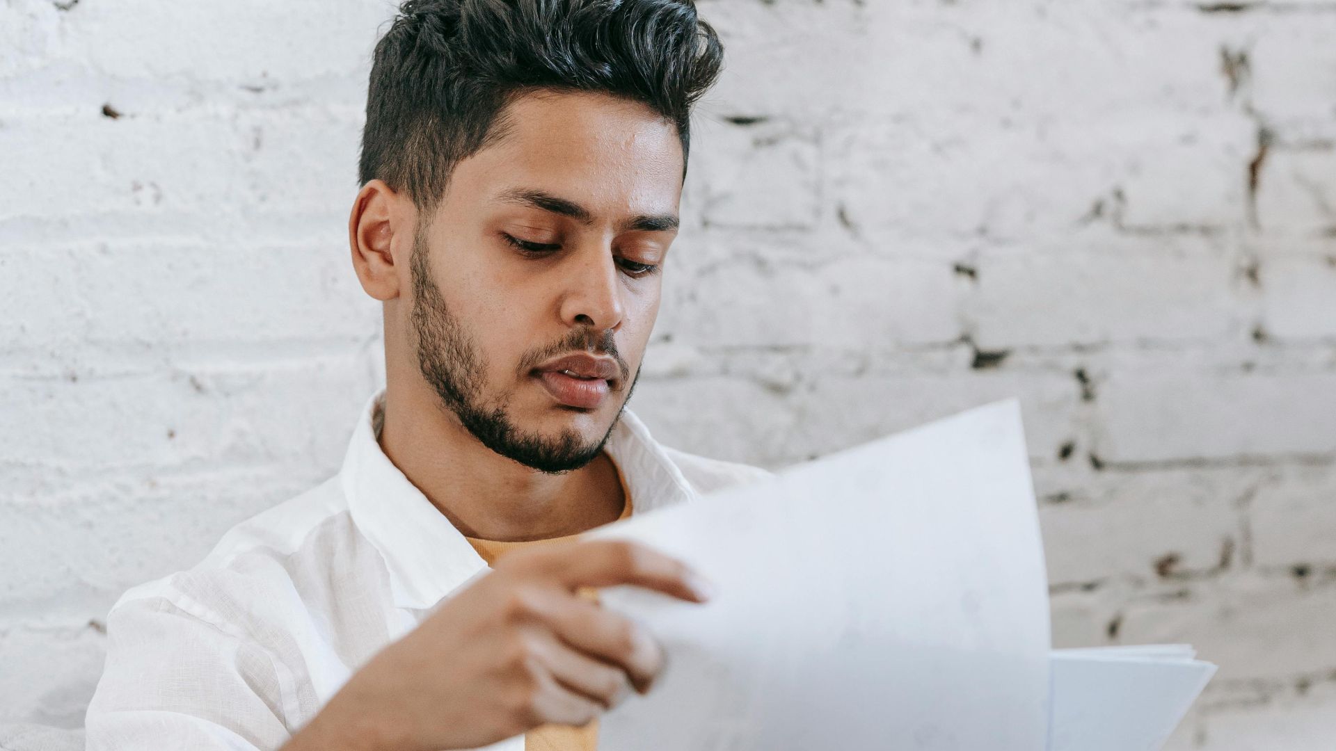 Concentrated young bearded Hispanic male sitting in armchair and analyzing contract while getting job offer