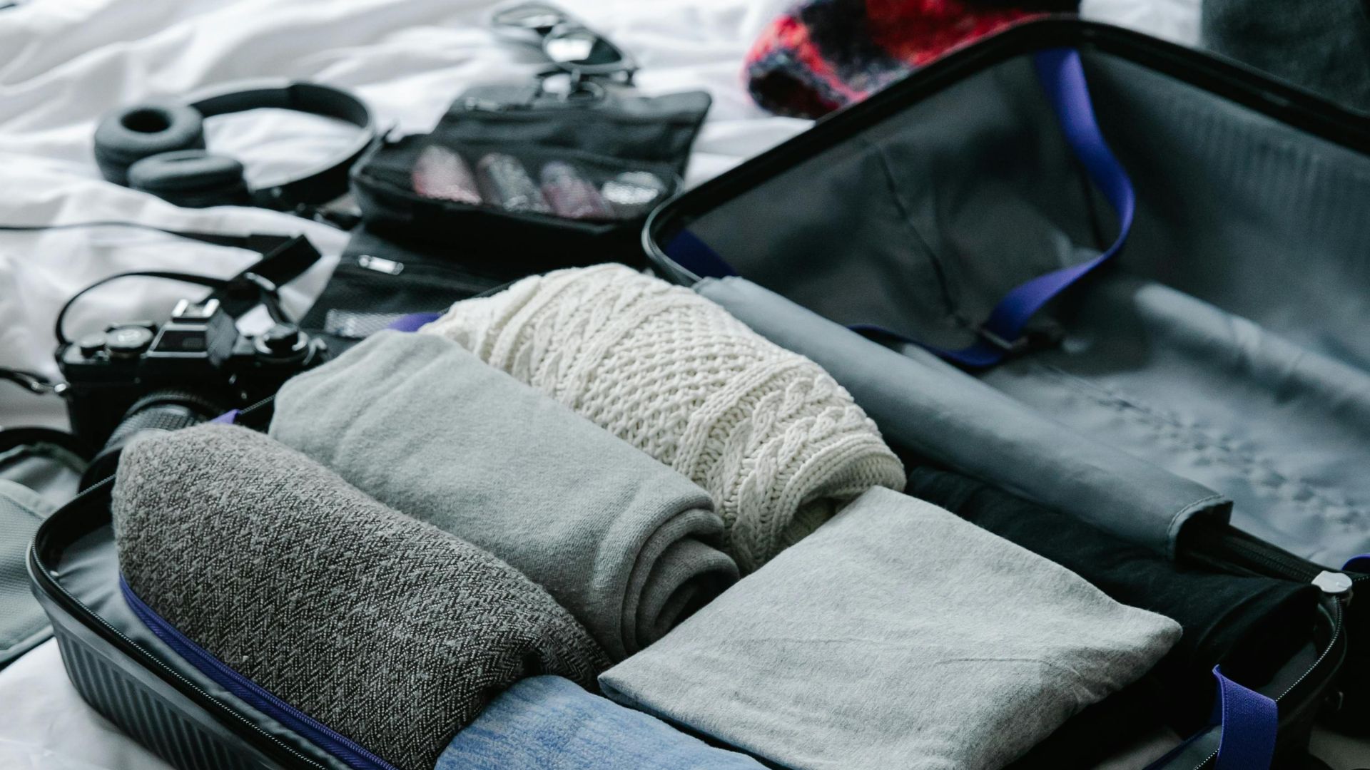 Open suitcase filled with neatly folded clothes on bed, ready for travel preparation.