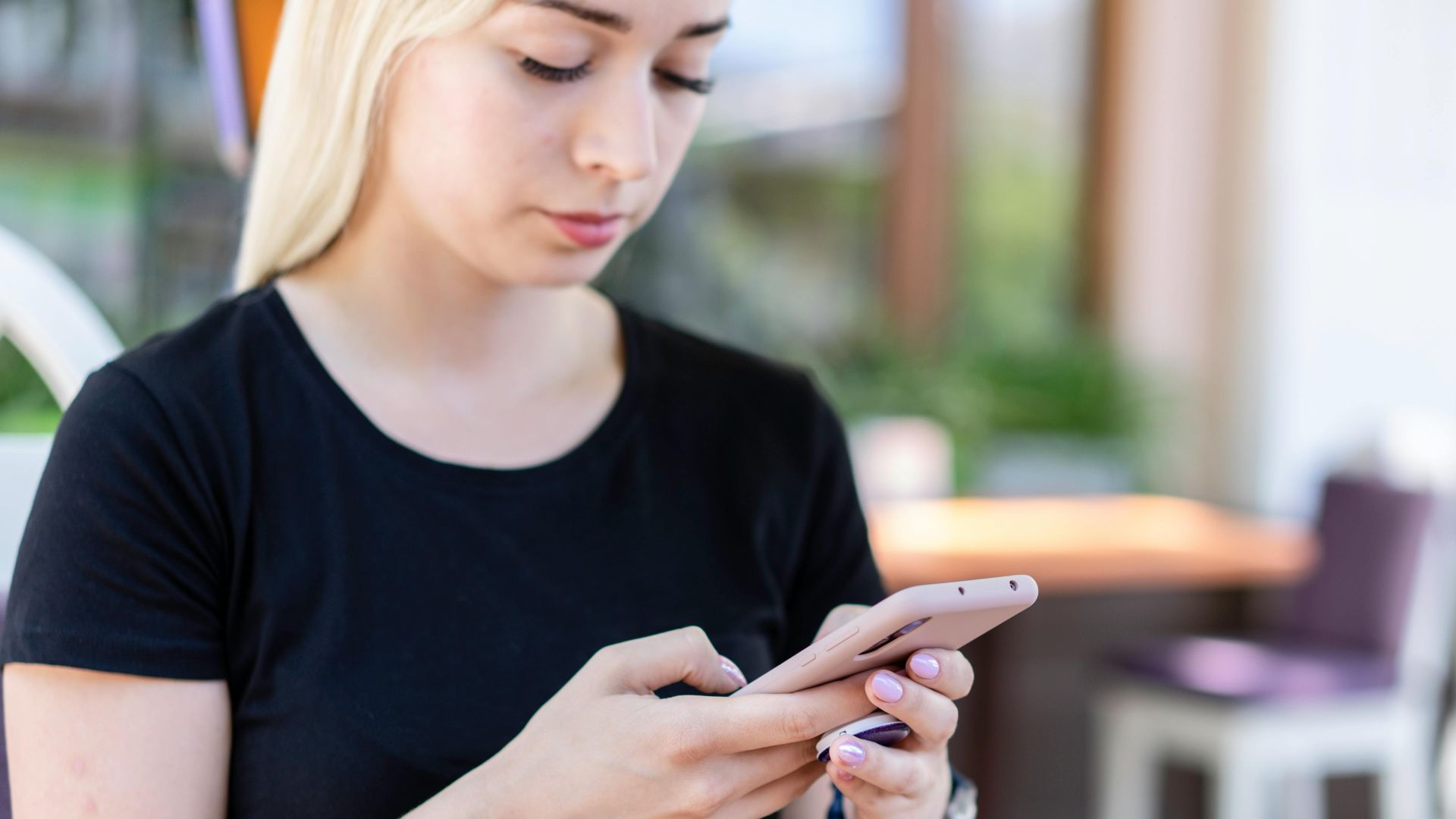 Young woman in a black shirt texting on her smartphone at an outdoor cafe.