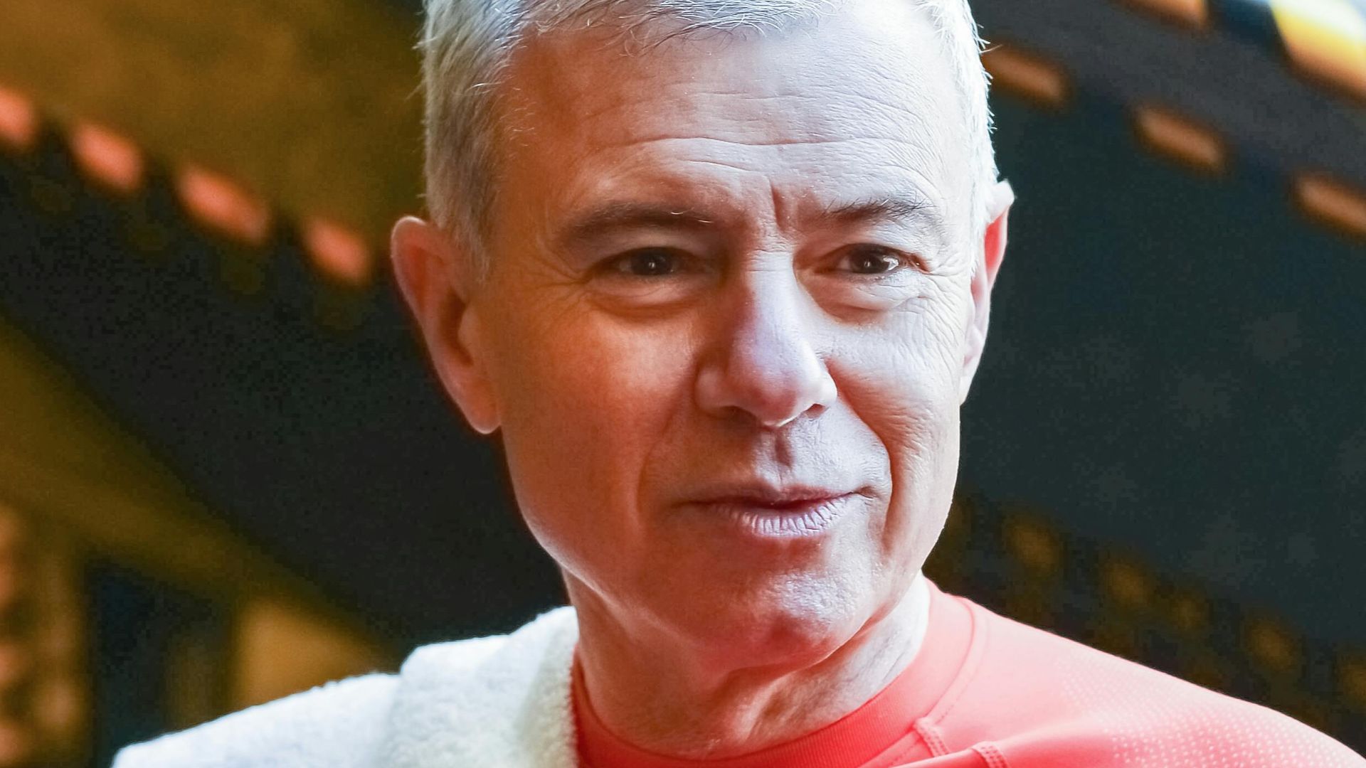 Senior man wearing activewear talking while holding a water bottle in a gym setting.