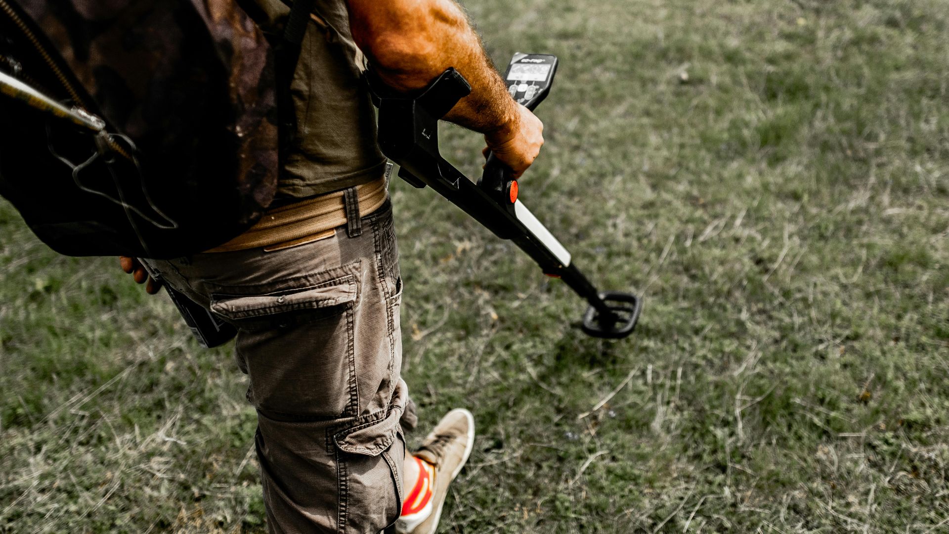 Person using a metal detector on a grassy field wearing casual attire.