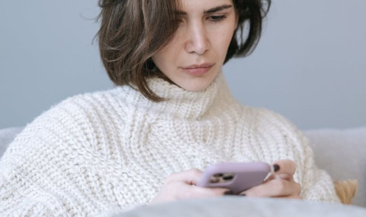 A Woman in White Knitted Sweater Using a Cellphone