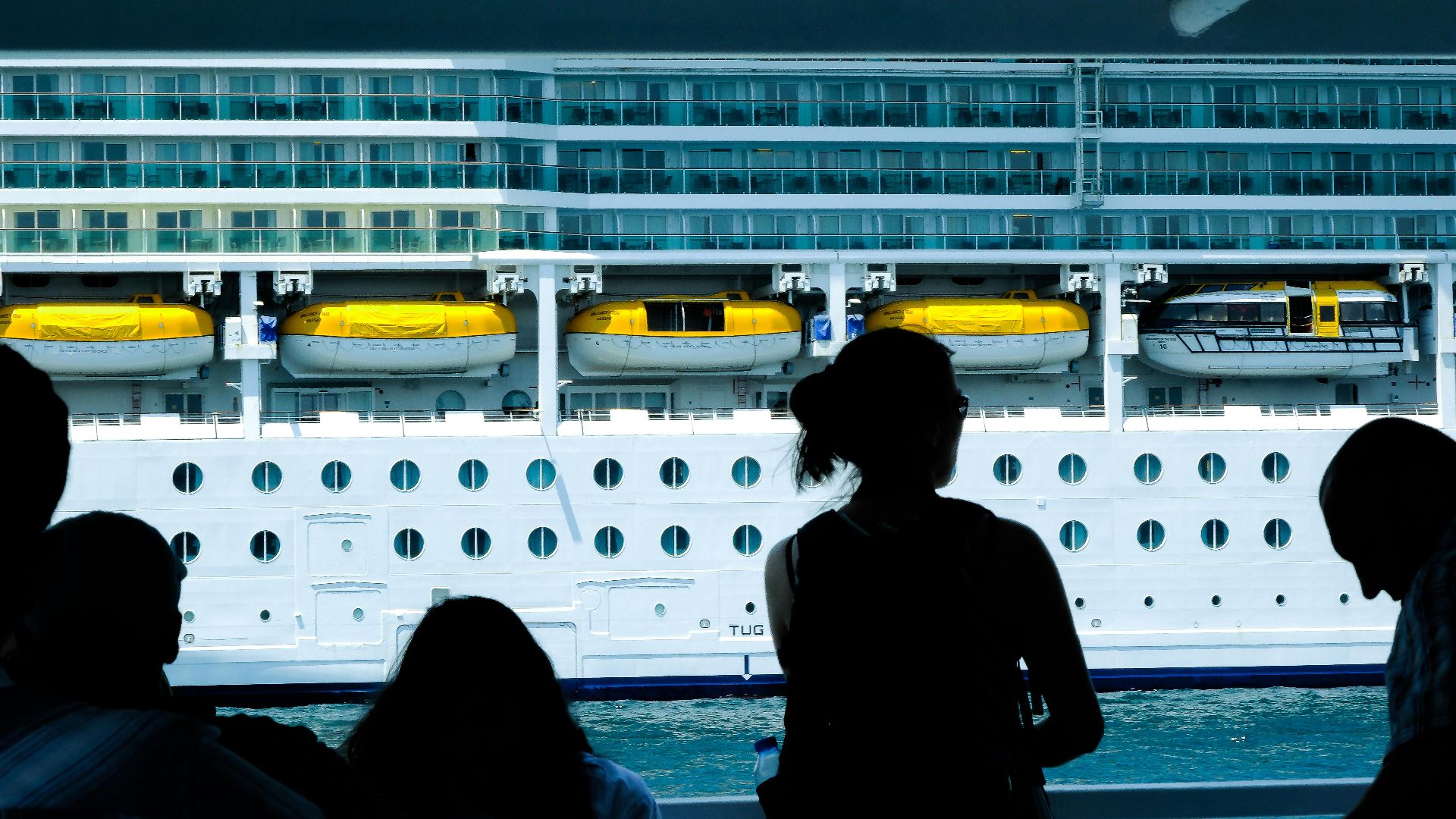 Silhouettes of people observing a large cruise ship from a dock in Türkiye.