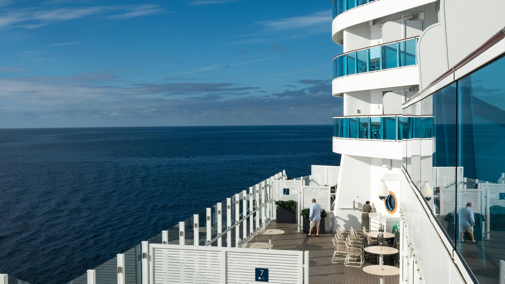 Scenic view of passengers enjoying a sunny day on a cruise ship deck overlooking the ocean.