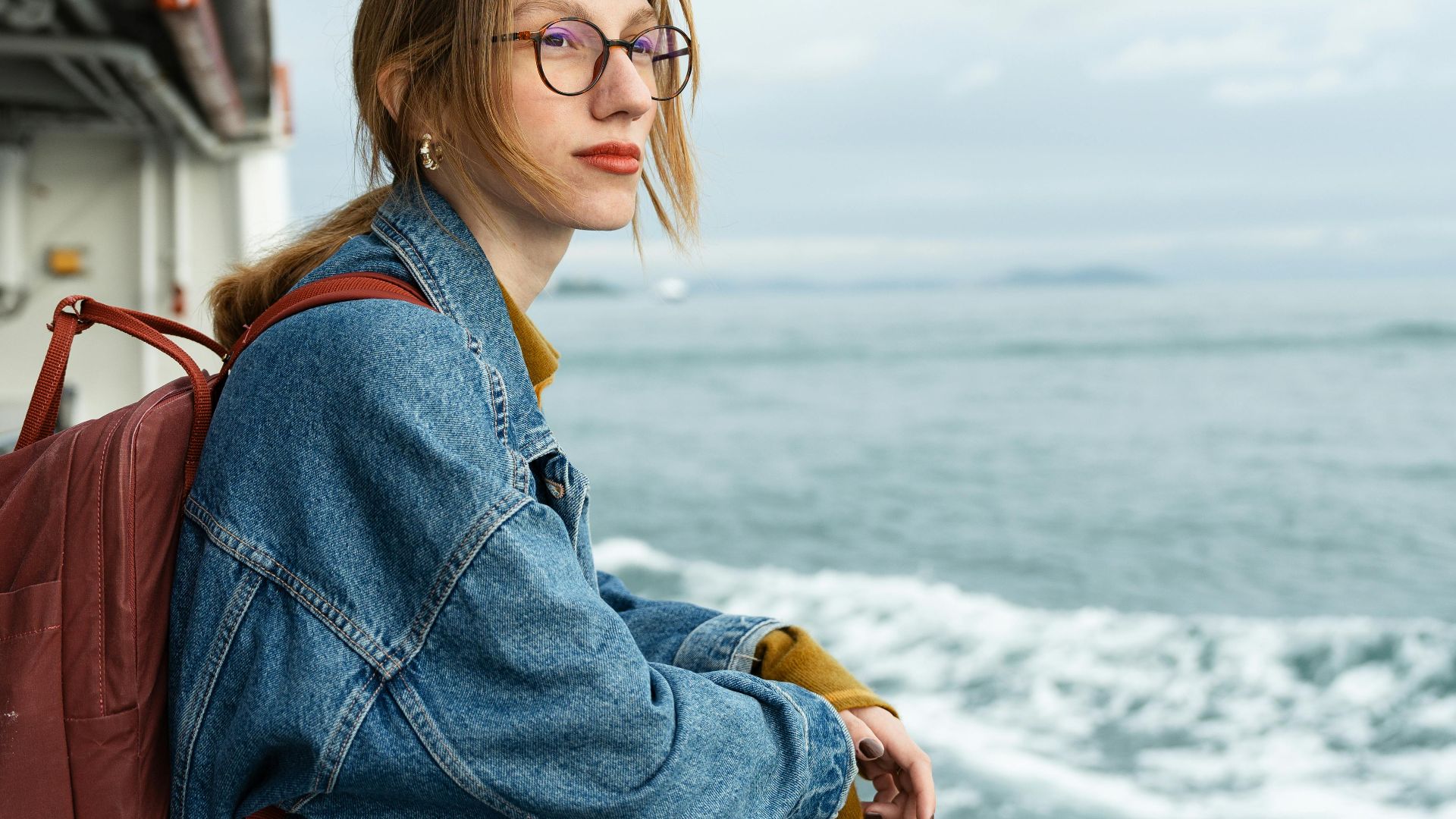 A woman with a backpack gazes at the ocean from a cruise ship deck, capturing a serene moment at sea.