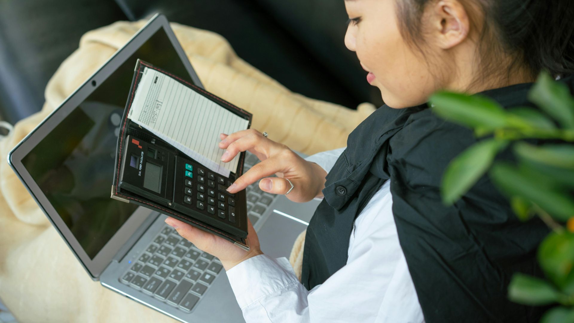 Focused young woman calculating finances on laptop indoors.