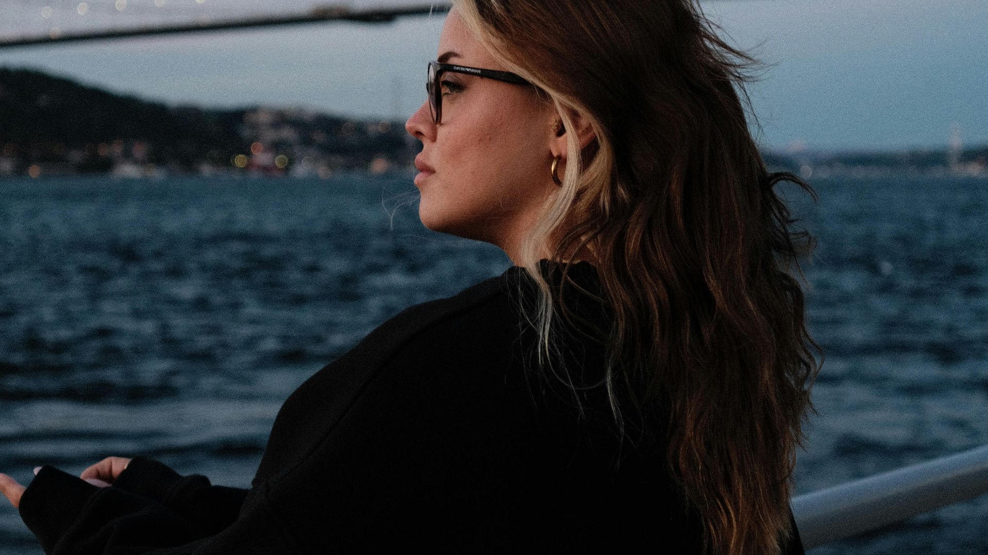 A woman stands thoughtfully by the Bosphorus Bridge at twilight, capturing the serene atmosphere.