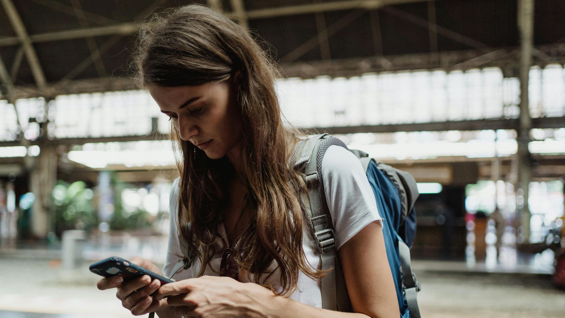 A young woman checks her smartphone while traveling at a train station.