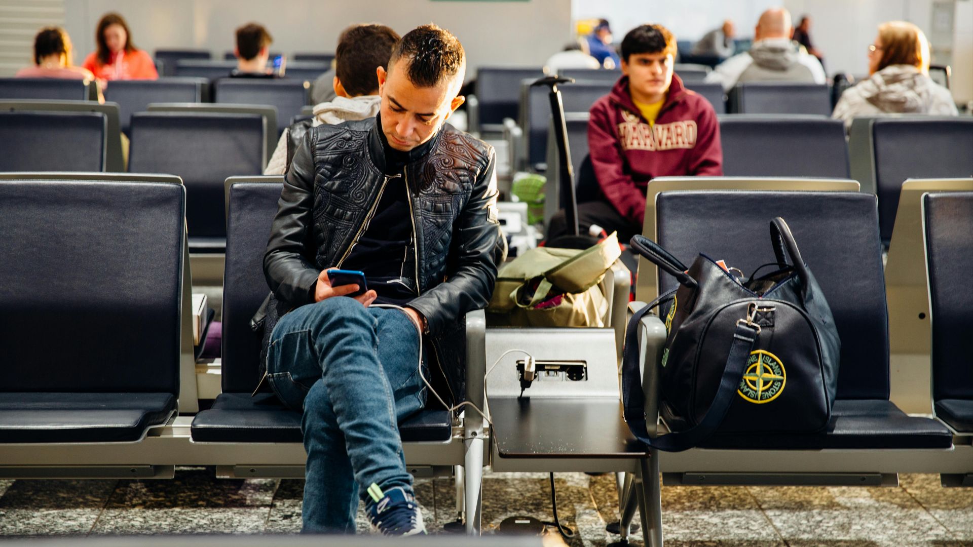 People sitting in an airport lounge, focused on smartphones and waiting for flights.