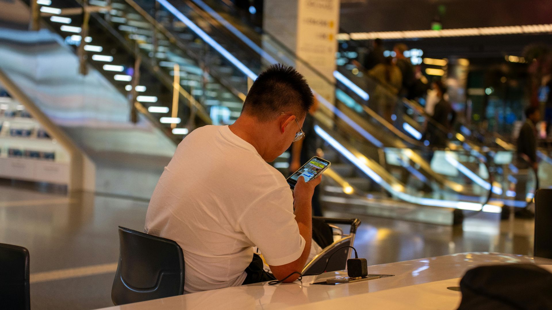 Adult using smartphone in modern airport terminal, Doha, Qatar. Busy travel scene with escalator.