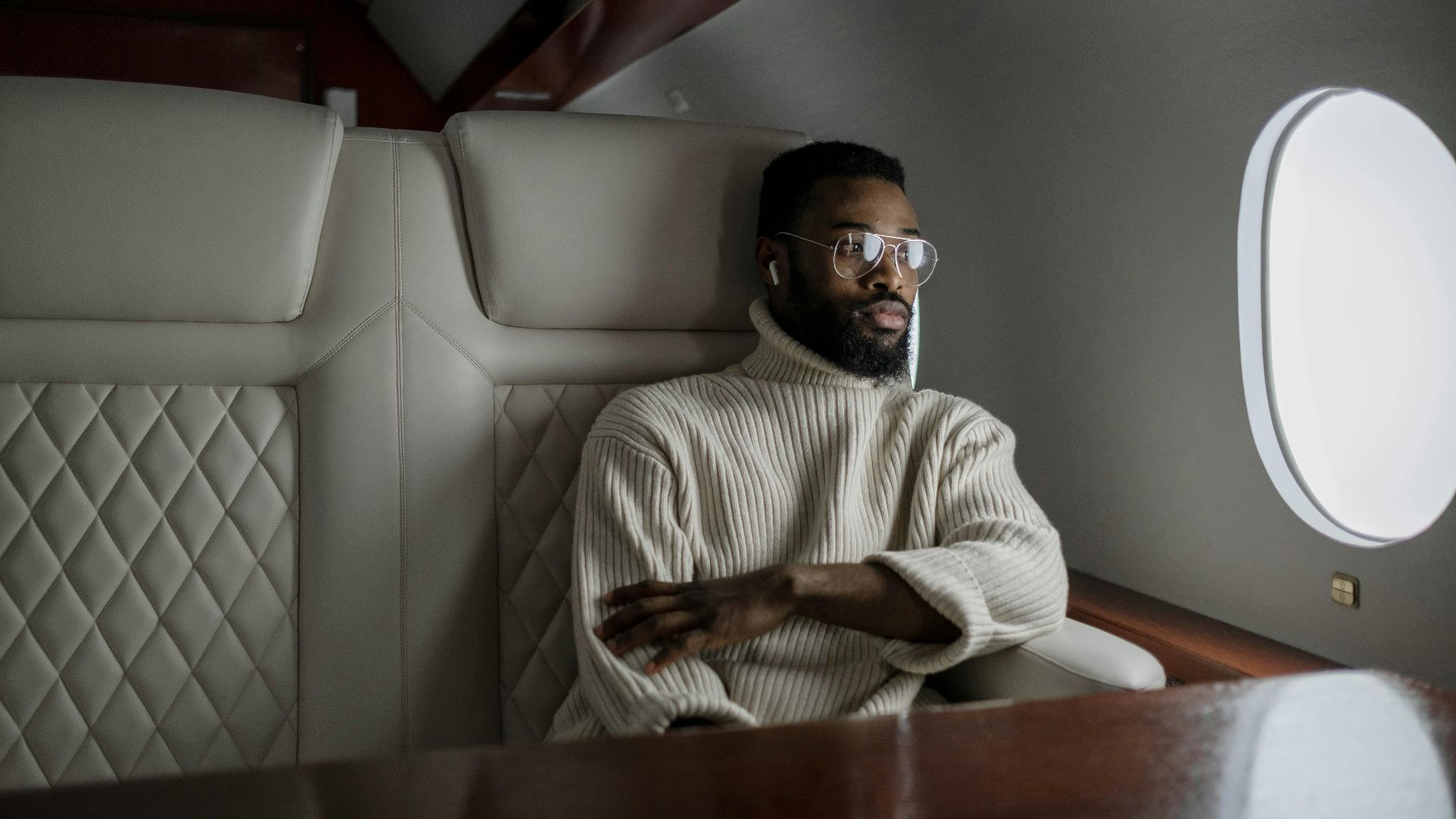 A stylish man in a turtleneck relaxes inside a private jet, embodying luxury travel.