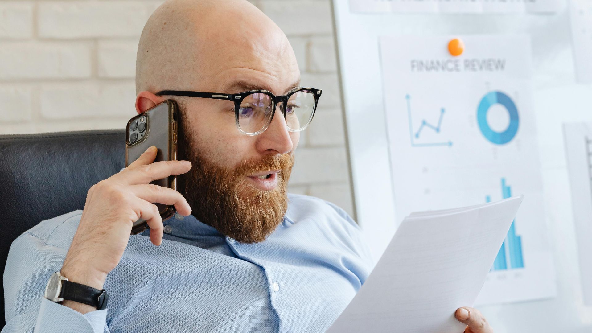 Professional analyzing data charts and graphs on paper and phone in office setting.