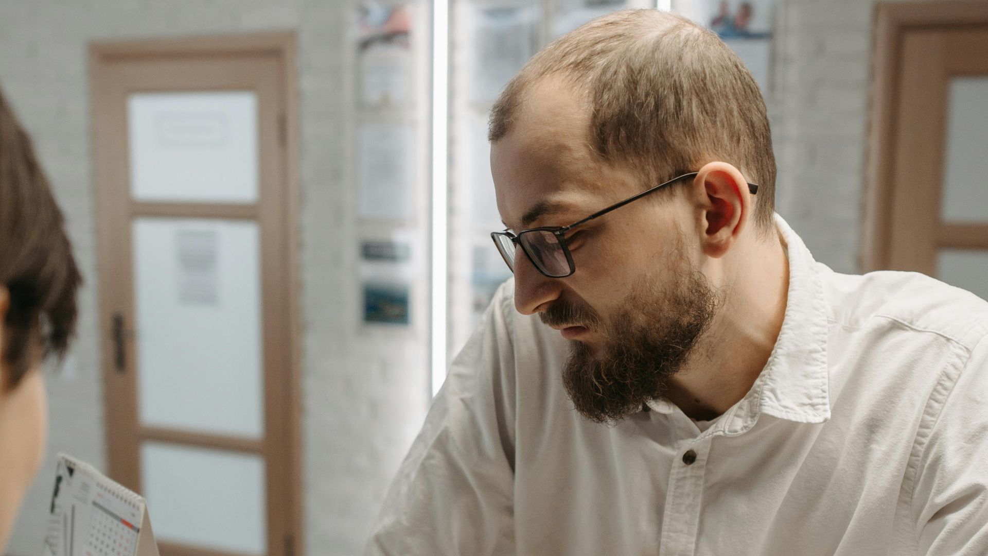A thoughtful man leaning on a reception counter while discussing plans indoors.