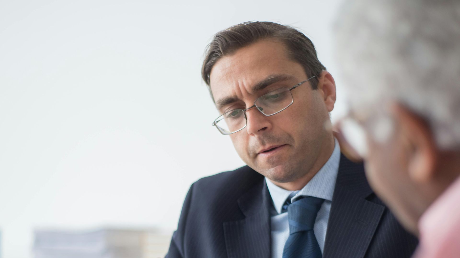 Senior man in discussion with consultant in office setting, reviewing documents.