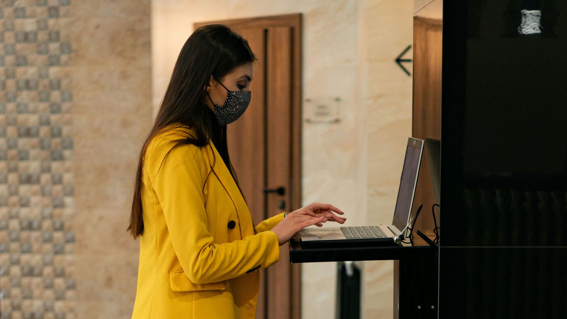 Business traveler using laptop at hotel reception with yellow suitcase.