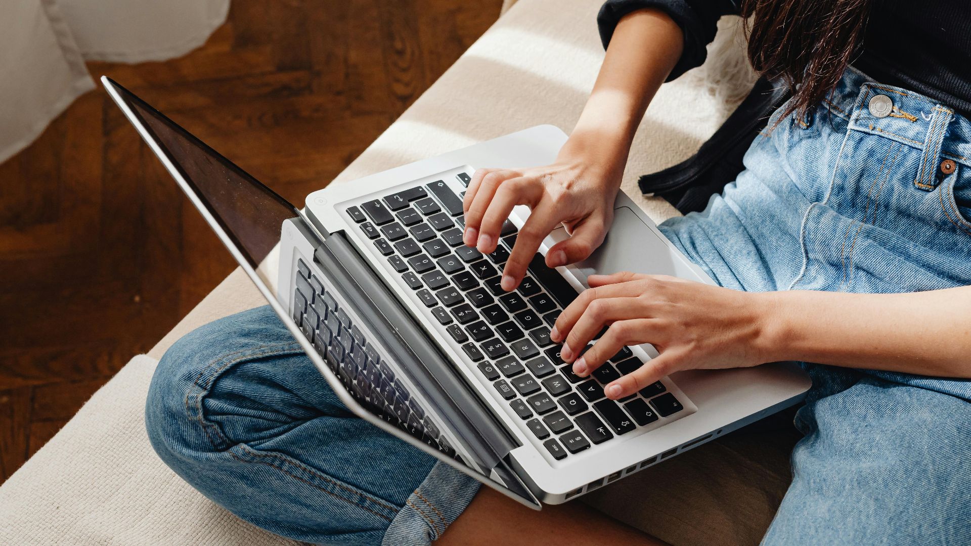 Close-up of a woman typing on a laptop, sitting cross-legged indoors.