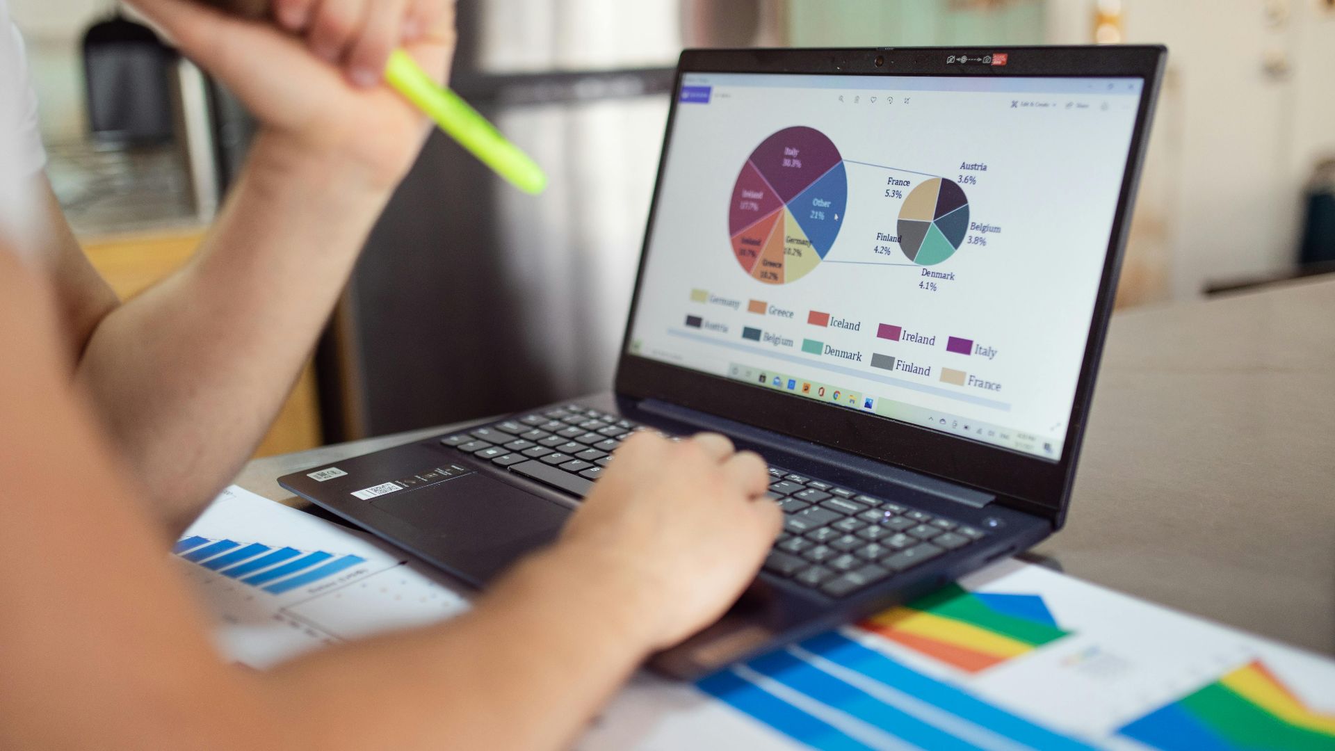 Person analyzing financial charts and graphs on a laptop with colorful documents, showcasing market analysis.
