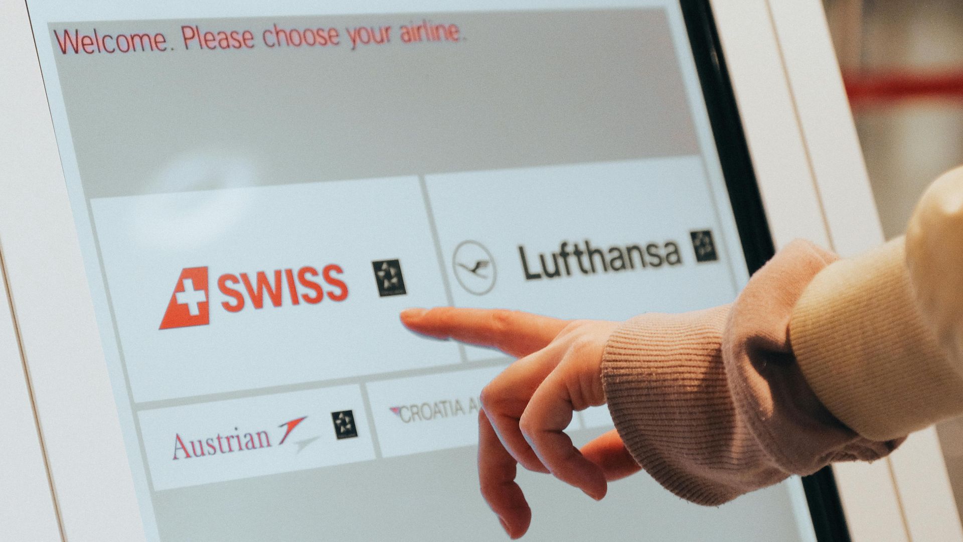 Hand interacting with airport kiosk for airline selection. Modern travel technology.