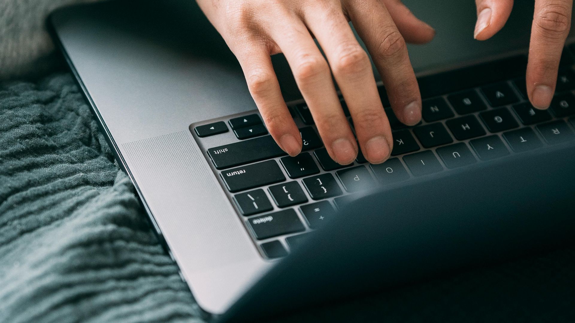 From above crop unrecognizable black person working and typing information on netbook on sofa