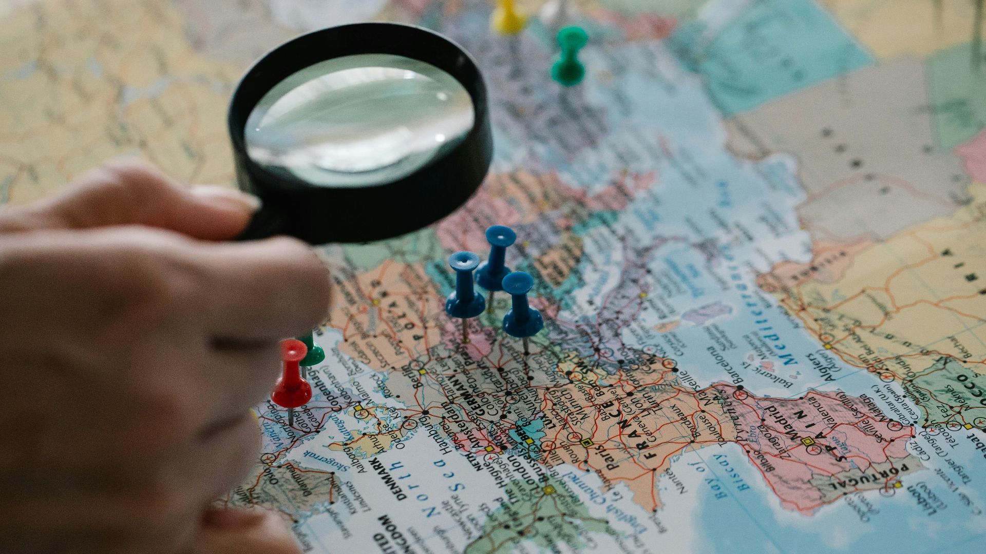 Magnifying glass focuses on pins highlighting travel destinations on a world map.