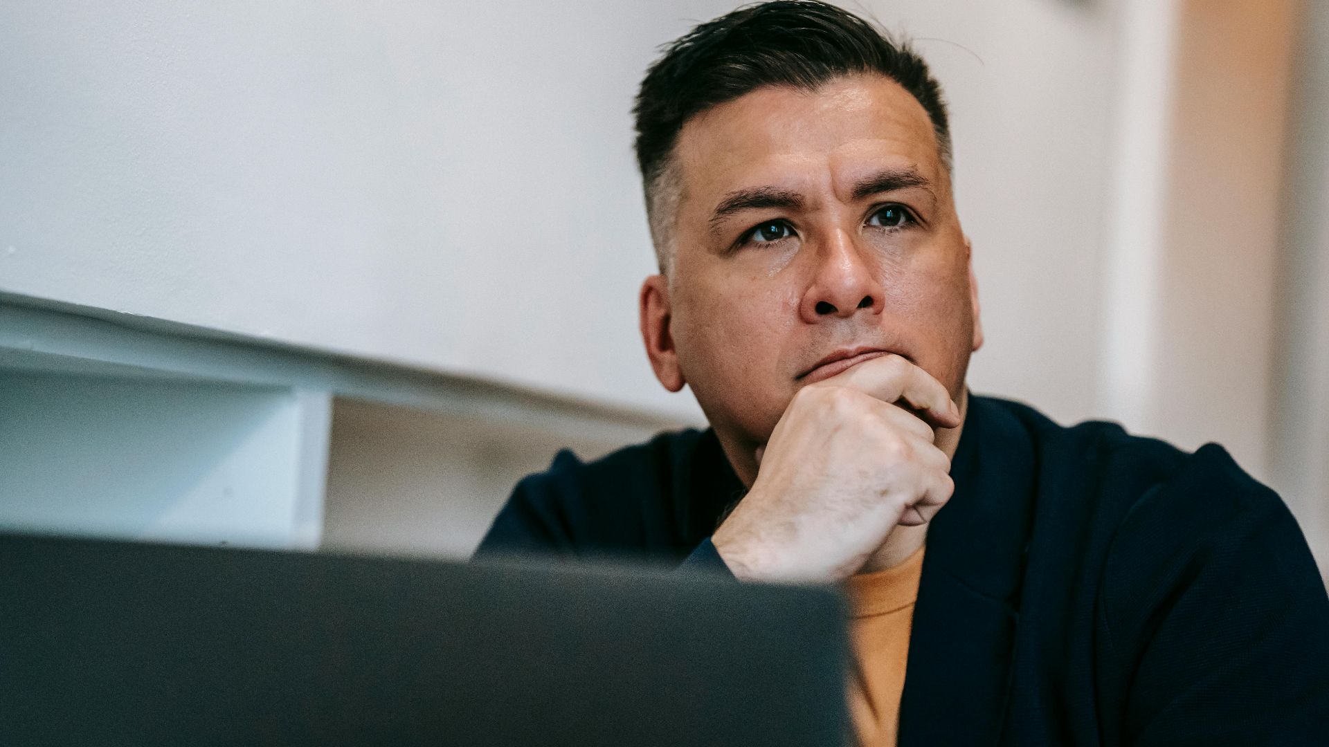 Focused man in home office pondering work on a laptop, expressing deep concentration and thought.