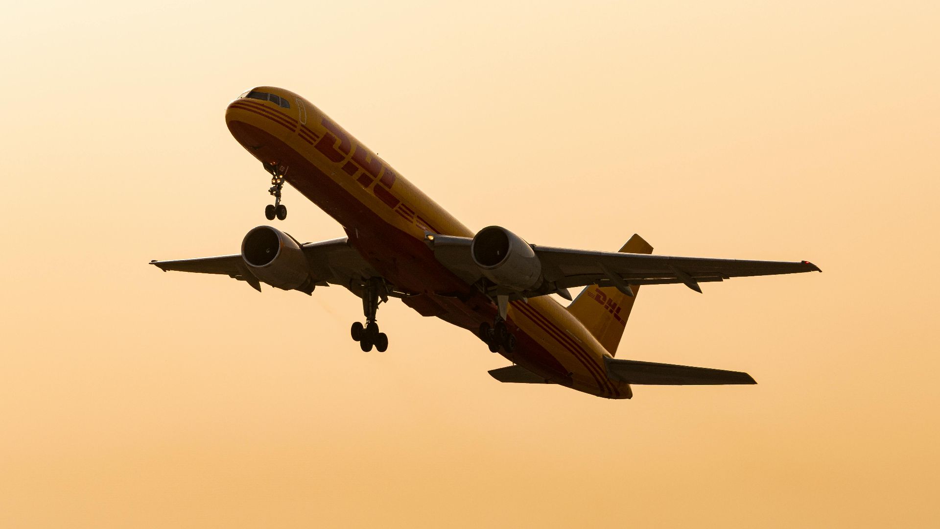 Cargo airplane flying in silhouette against a warm sunset sky.