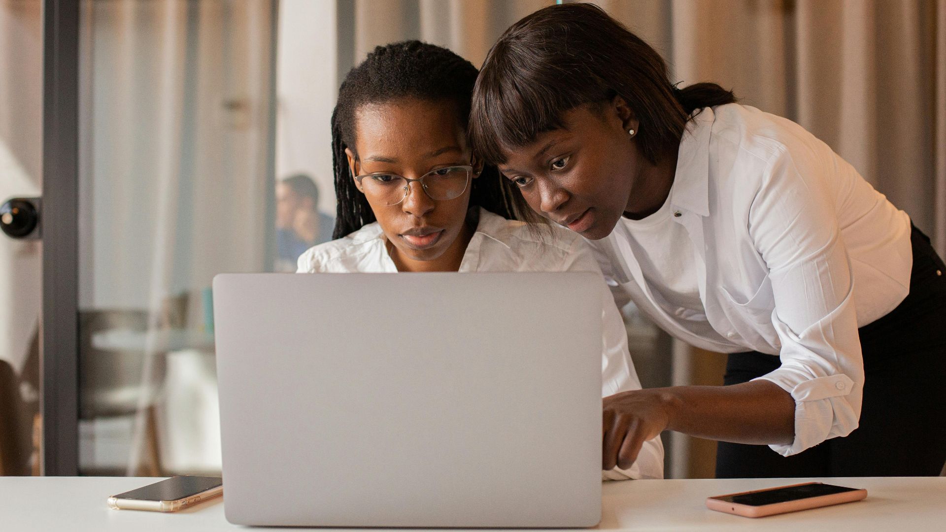 Two African American women working together on a laptop indoors, showcasing teamwork and collaboration.